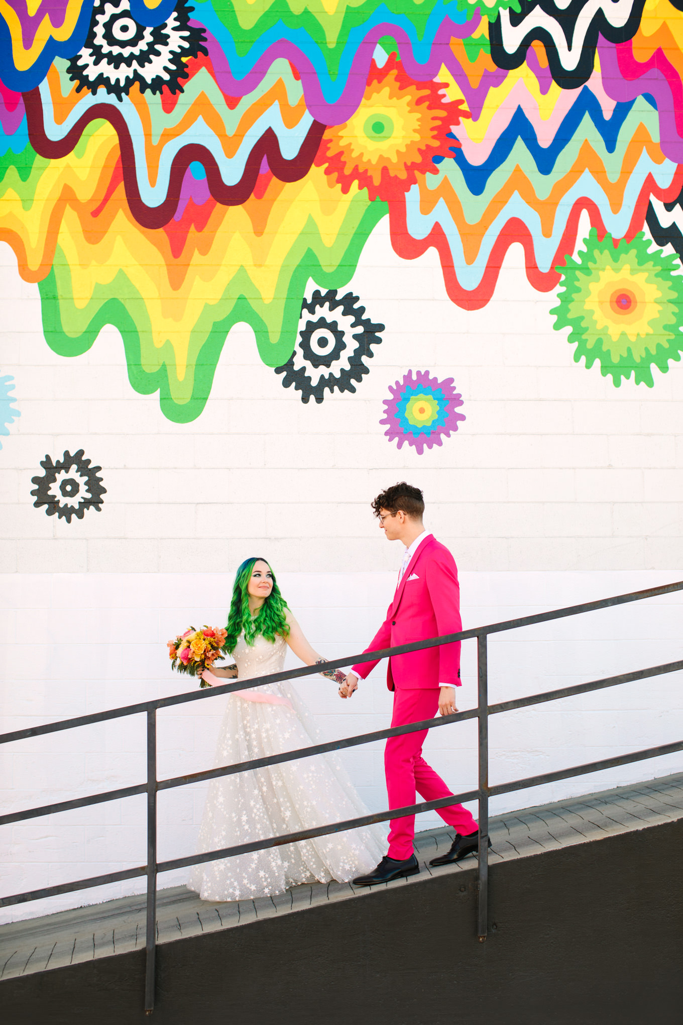 Bride with green hair and groom in pink suit in front of rainbow mural DTLA | Colorful wedding at The Unique Space Los Angeles published in The Knot Magazine | Fresh and colorful photography for fun-loving couples in Southern California | #colorfulwedding #losangeleswedding #weddingphotography #uniquespace Source: Mary Costa Photography | Los Angeles