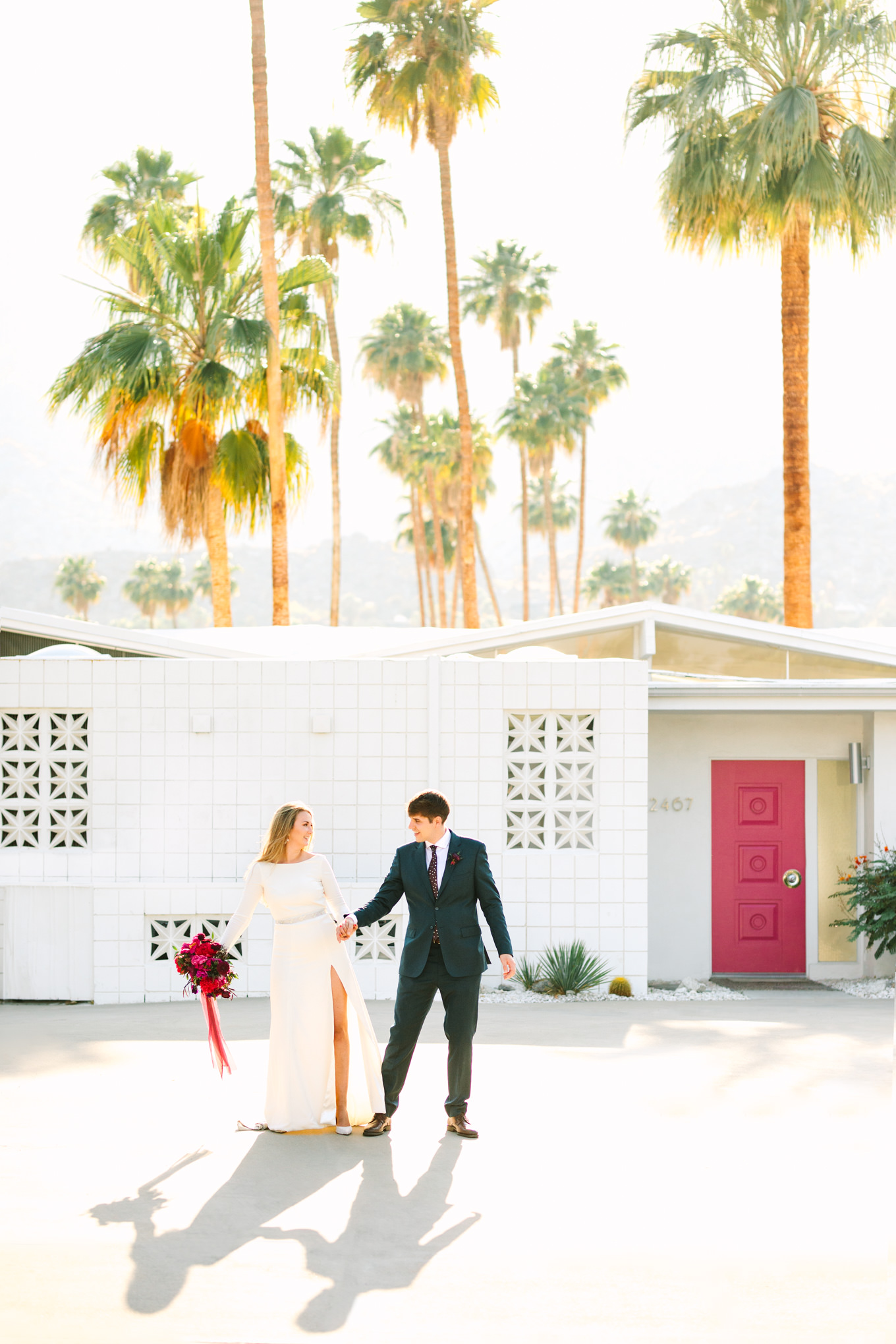 Bride and groom walking in Mid-Century Modern neighborhood with pink door | Colorful jewel tone Palm Springs elopement | Fresh and colorful photography for fun-loving couples in Southern California | #colorfulelopement #palmspringselopement #elopementphotography #palmspringswedding Source: Mary Costa Photography | Los Angeles