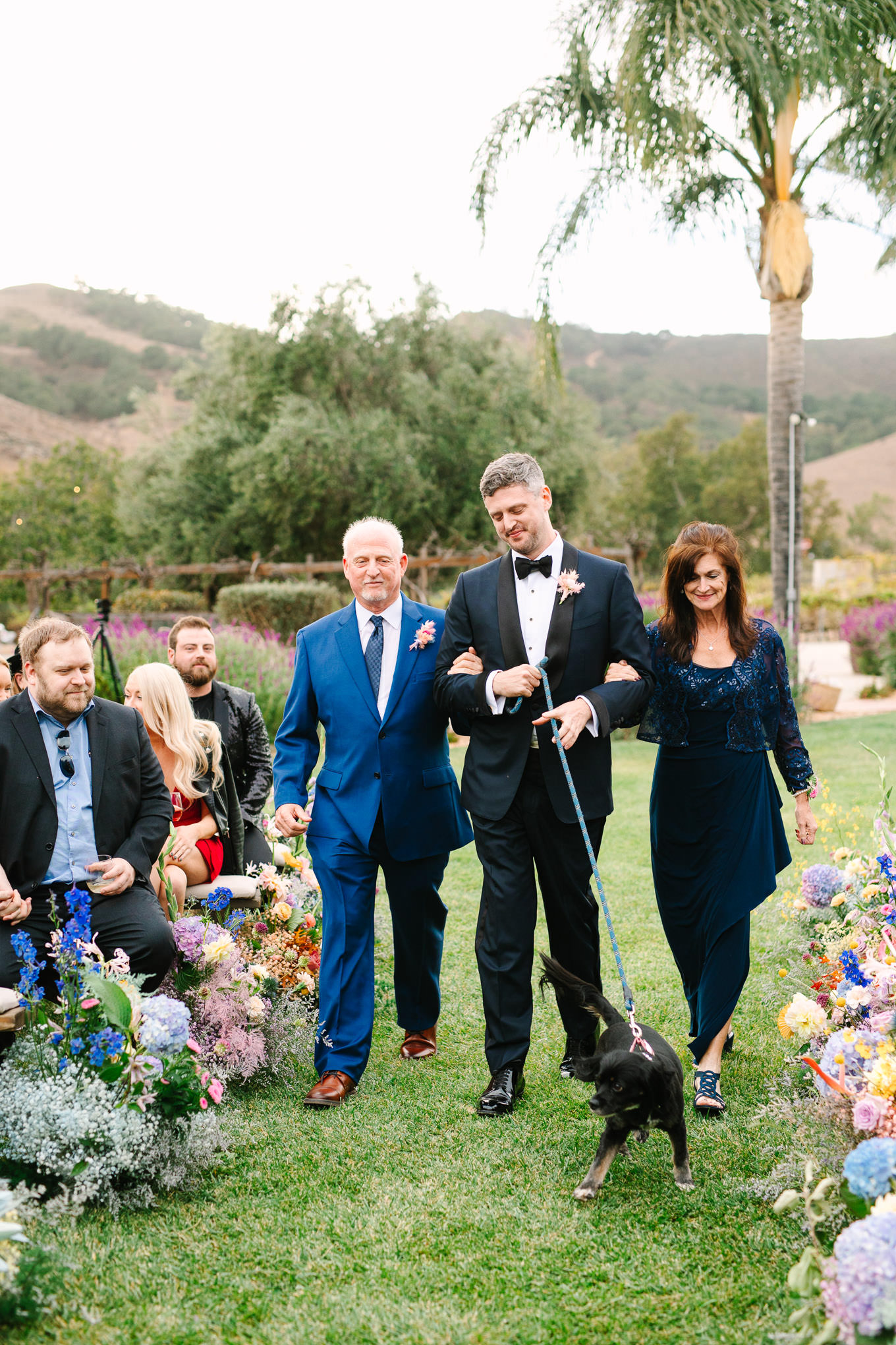 Groom walking with parents and dog at wedding ceremony | Colorful and quirky wedding at Higuera Ranch in San Luis Obispo | #sanluisobispowedding #californiawedding #higueraranch #madonnainn   Source: Mary Costa Photography | Los Angeles