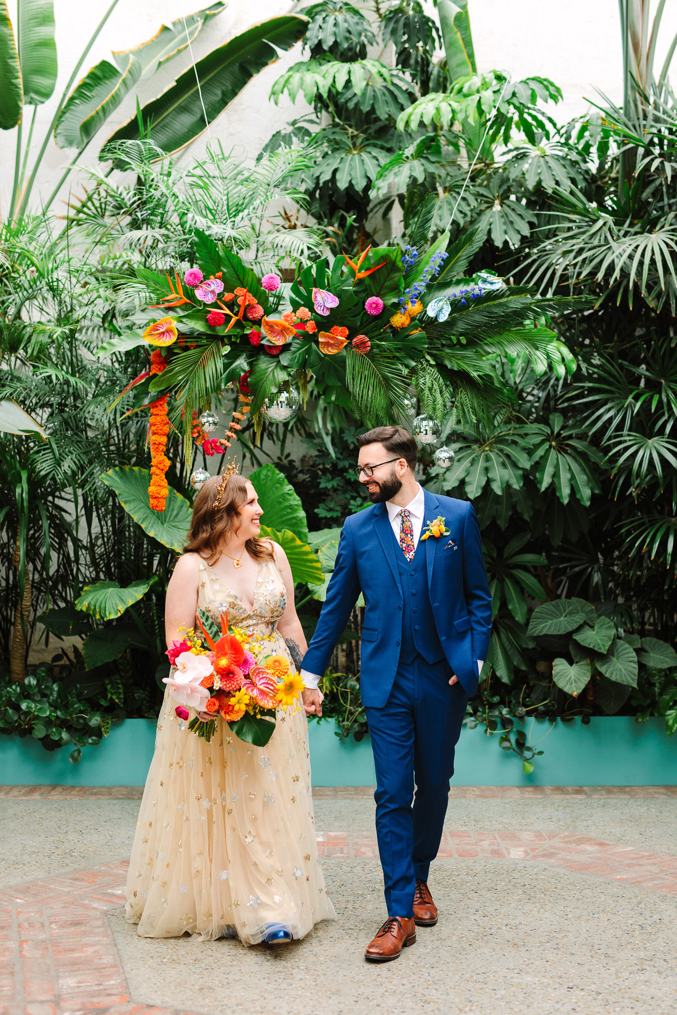Bride and groom walking in front of tropical backdrop with disco balls | Colorful Downtown Los Angeles Valentine Wedding | Los Angeles wedding photographer | #losangeleswedding #colorfulwedding #DTLA #valentinedtla   Source: Mary Costa Photography | Los Angeles